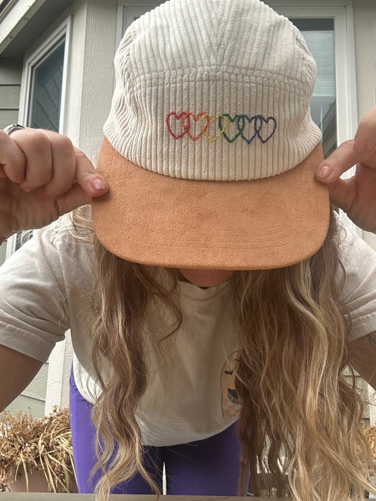 Person wearing corduroy cream hat with rainbow hearts